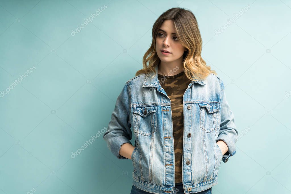 Fashionable young woman wearing denim jacket looking away against blue background