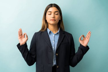 Female professional in suit gesturing while meditating against isolated background