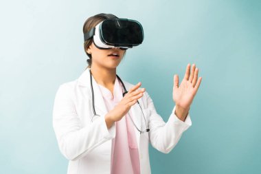 Hispanic medical surgeon wearing virtual reality glasses gesturing against colored background
