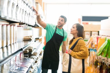 Confident male owner showing various food products on shelf to female consumer in store