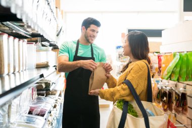 Smiling male owner giving paper bag to female customer and selling food in bulk in supermarket