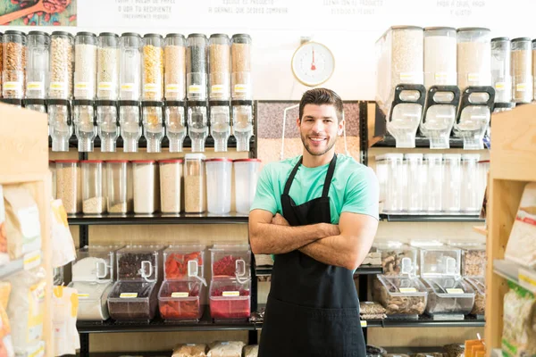 Confident Hispanic Male Owner Standing Arms Crossed Bulk Food Aisle — 스톡 사진