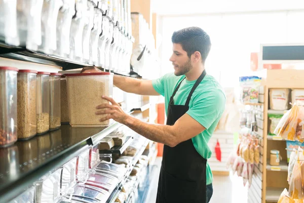 スーパーの棚に食品容器を並べラテン男性営業担当者の側面図 — ストック写真