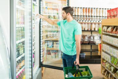 Side view of young man removing drink from refrigerator while shopping in grocery store