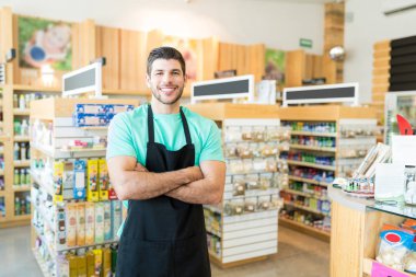 Confident Latin male owner standing with arms crossed in grocery store