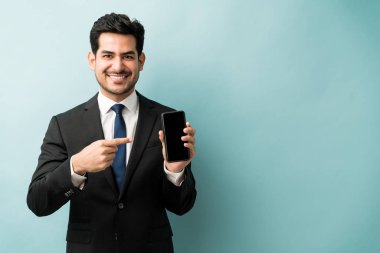 Portrait of confident young male professional pointing at smartphone while standing against isolated background