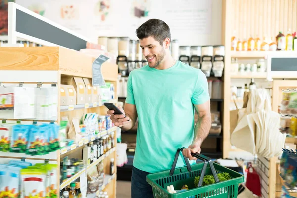 Hispanic Young Man Smiling While Text Messaging Smartphone Grocery Store — Stock Photo, Image