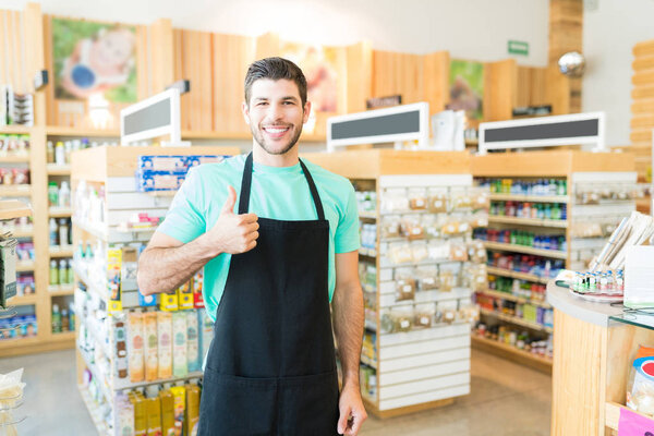 Smiling Hispanic male owner standing with thumbs up in grocery store