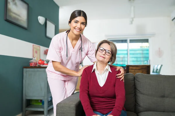 Portrait Confident Nurse Elderly Woman Sitting Sofa Home — Stockfoto