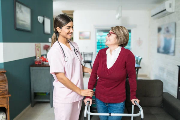 Улыбающаяся Медсестра Помогает Пожилой Женщине Ходить Инвалидом Дома — стоковое фото