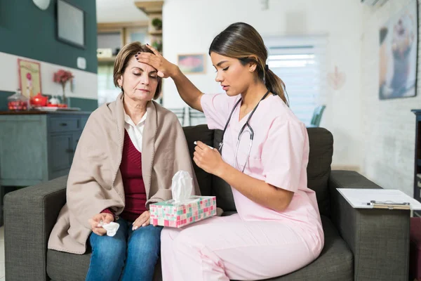 Female Nurse Checking Fever Senior Woman While Sitting Sofa Home — Stock Photo, Image