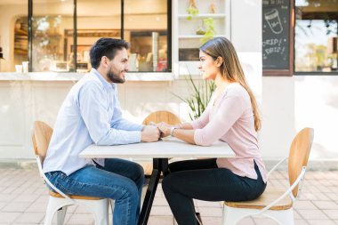 Gülümseyen sevgili ve kız arkadaşın kaldırımdaki kafede el ele tutuşması.