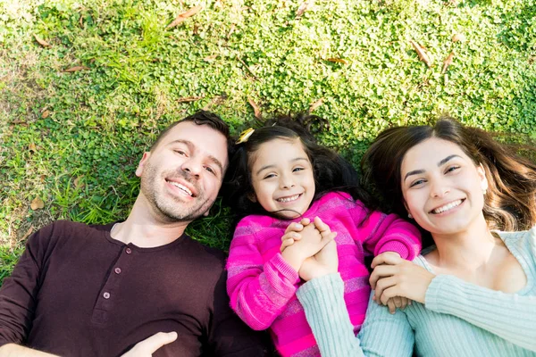 公園で草の上に横たわる幸せなヒスパニック系の家族の頭上の肖像画 — ストック写真