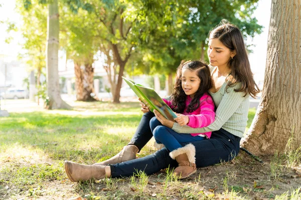 Young Mother Reading Picture Book Daughter While Sitting Tree Park — Stock Photo, Image