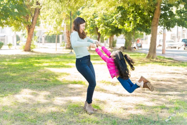 晴れた週末に公園で手をつないでいる間にヒスパニック系の陽気な母親が娘をスイング — ストック写真