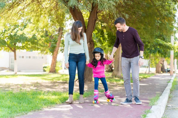 西班牙裔父亲和母亲牵着女儿的手 同时指导她在人行道上滑冰 — 图库照片