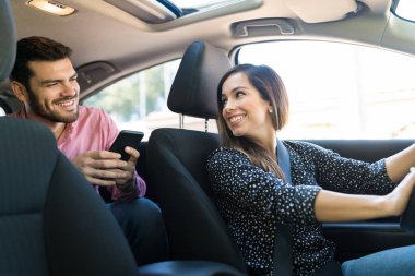 Smiling confident female driver talking with male customer in taxi