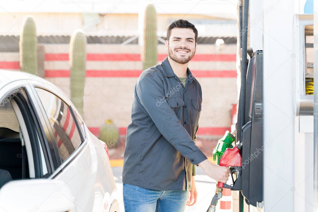 Portrait of smiling male staff holding fuel pump at gas station