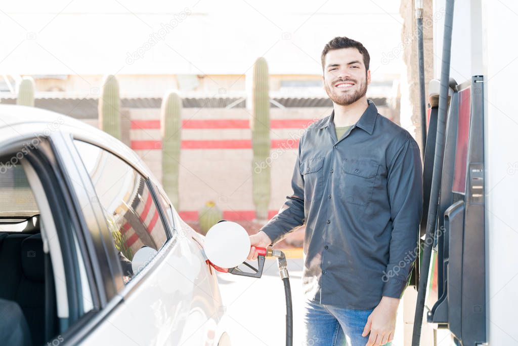 Confident male worker in uniform refueling car at gas station