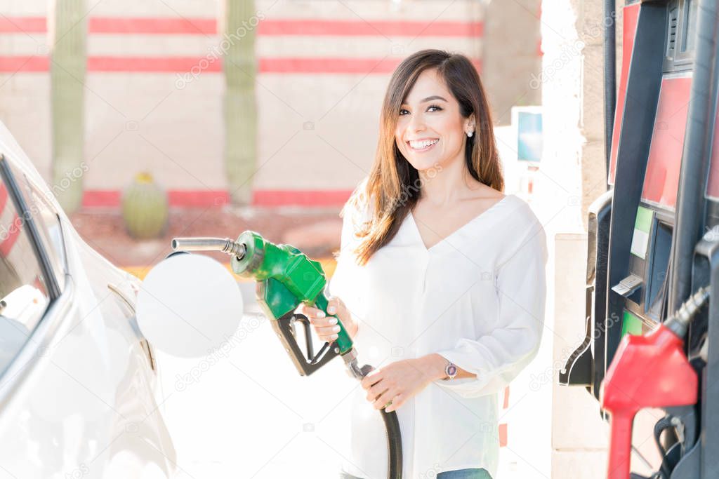 Happy mid adult woman holding fuel pump by car at self-service gas station