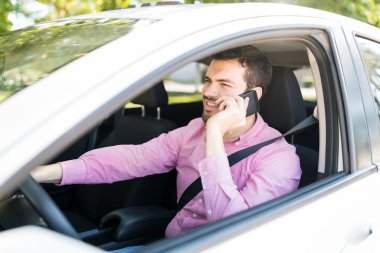 Gülümseyen yetişkin bir adam arabada otururken cep telefonuyla konuşuyor.