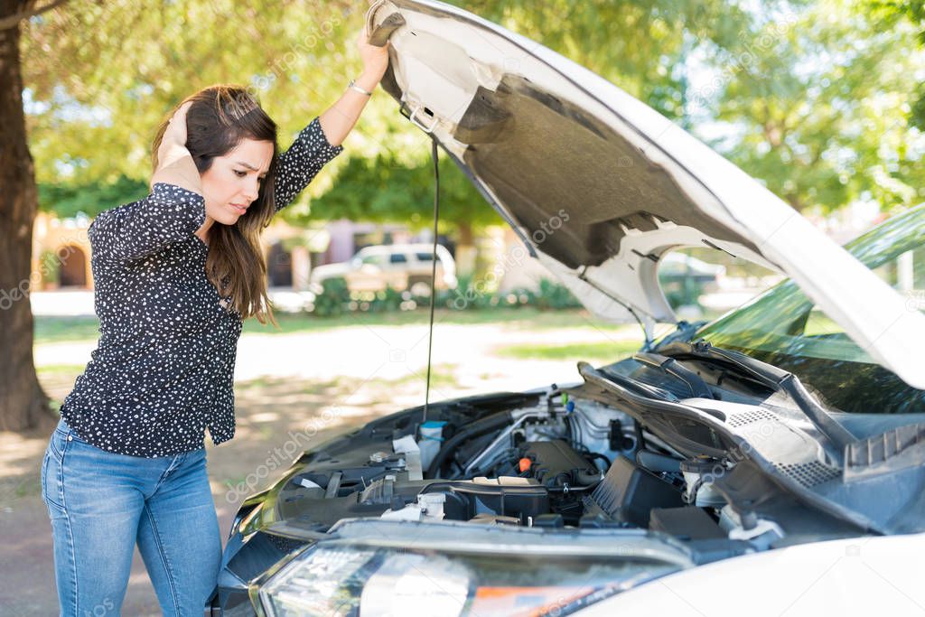 Unhappy woman looking at engine of broken car at roadside