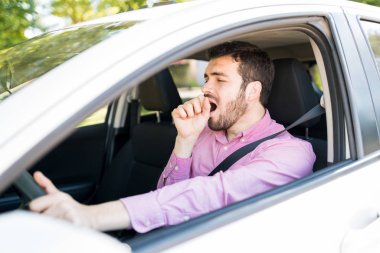 Bored Hispanic man yawning while waiting in car during traffic