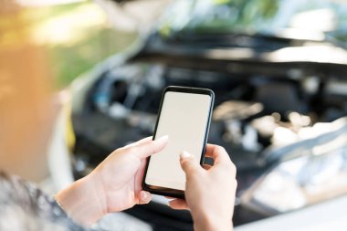 Bozuk arabanın yanında dururken elinde boş ekran olan akıllı telefonu tutan kadın.