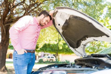 Good looking Latin adult man looking at engine of broken car