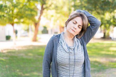 Yaşlı kadın kollarını kaldırarak boynunu uzatıyor ve gözleri kapalı duruyor.