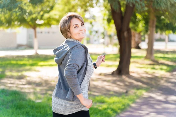 Smiling Retired Senior Woman Running Sidewalk While Looking Back Shoulder — Stock Photo, Image