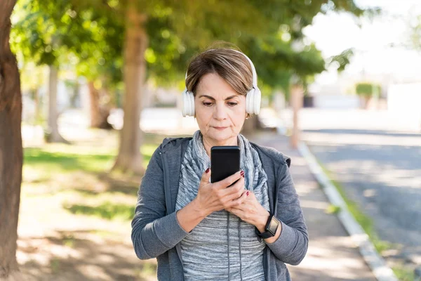 Wanita Senior Yang Percaya Diri Menggunakan Smartphone Sambil Mendengarkan Melalui — Stok Foto