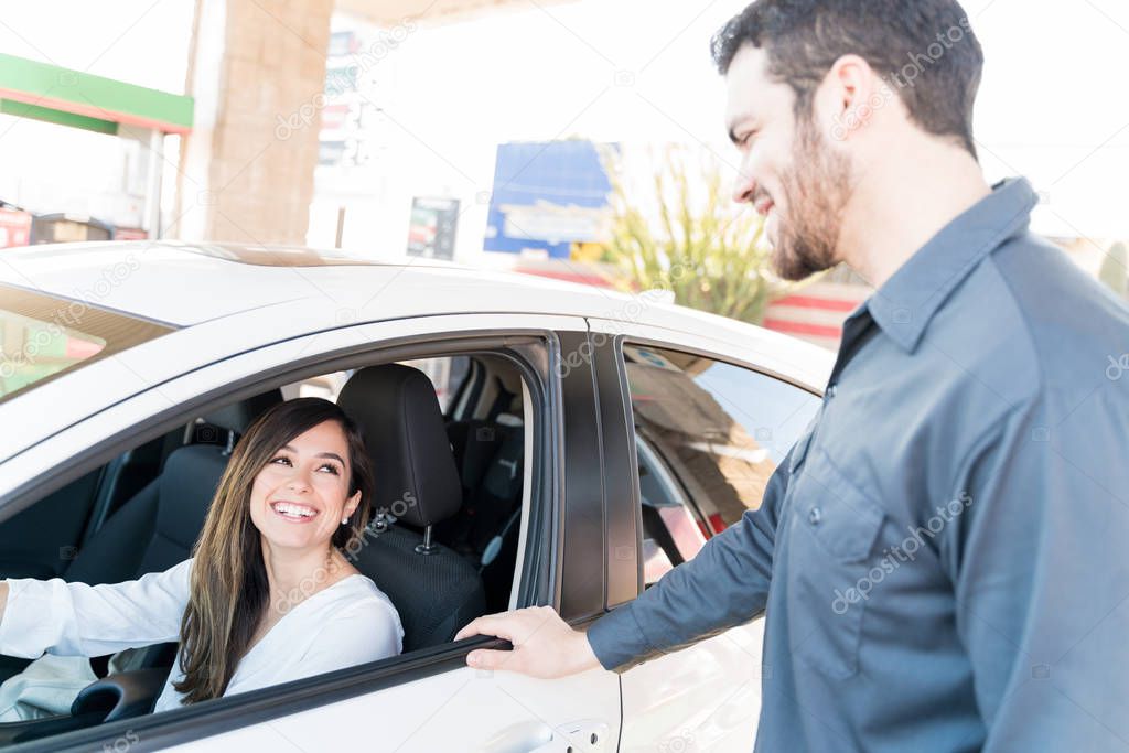 Smiling woman talking with male attendant at gas station while sitting in car