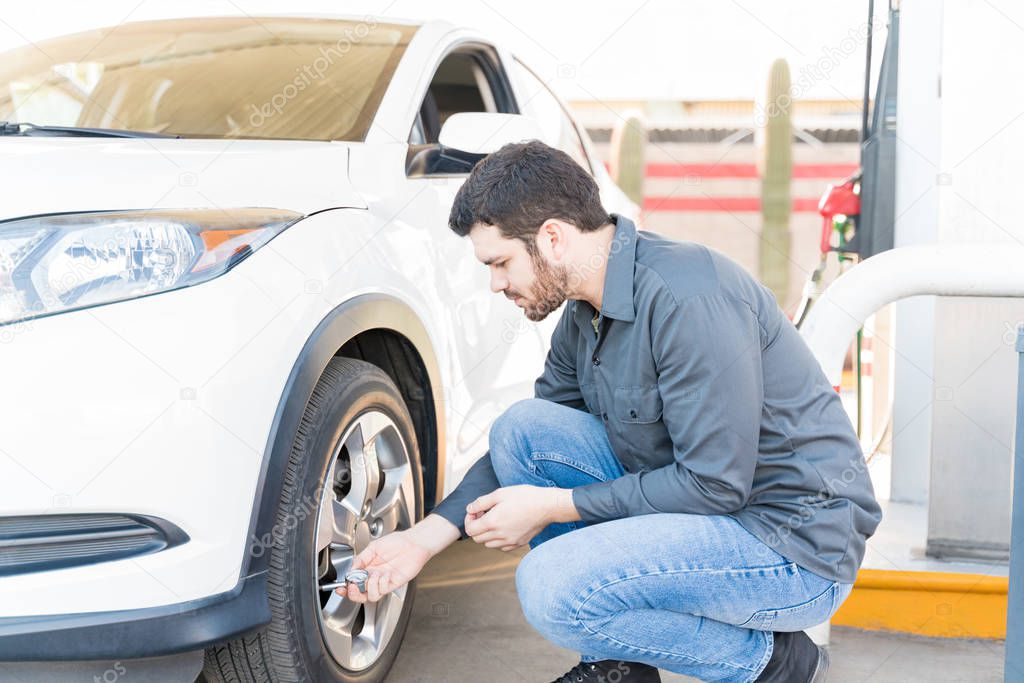 Side view of male gas station attendant checking air pressure of car tire