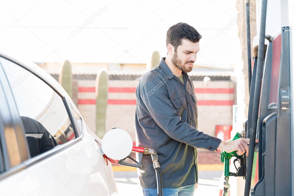 Male worker operating fuel pump machine at gas station