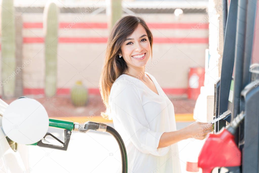Portrait of happy woman operating fuel pump machine at gas station
