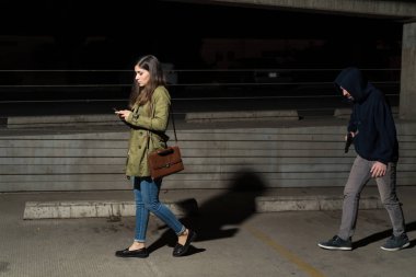 Gece otoparkta soyguncu tarafından takip edilirken, farkında olmayan kadın kurbanın cep telefonu kullanışının yan görüntüsü