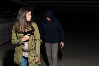 Karanlık otoparkta omzunun üzerinden hırsıza bakarken silahlı cesur bir kadın yürüyor.
