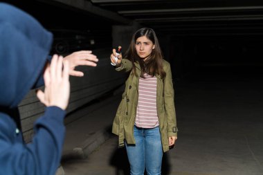 Kendini biber gazıyla savunan korkmuş bir kadın karanlık otoparkta duruyor.