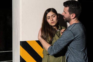 Hoşnut olmayan güzel bir kadın. Erkek arkadaşının kollarına sarılmış. Geceleri köşe yazısına karşı.