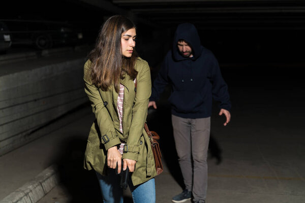 Attentive woman with gun walking ahead of criminal in dark parking lot