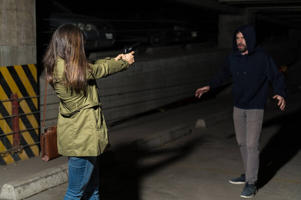 Woman pointing gun at criminal standing in dark parking lot