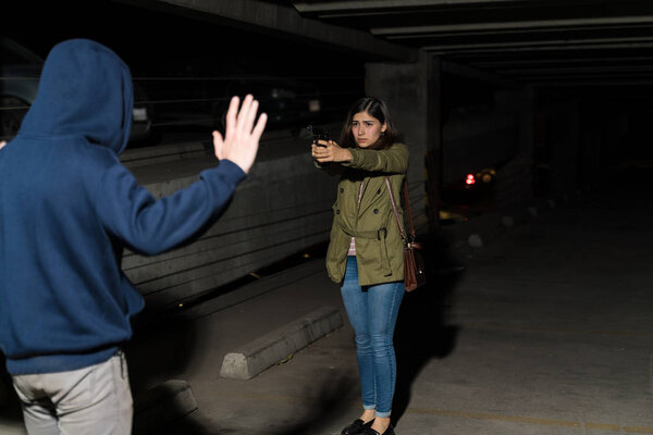 Scared female victim pointing gun at thief standing in dark parking lot
