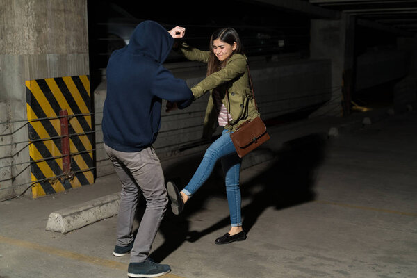 Full length of Latin woman fighting against robber in dark parking lot