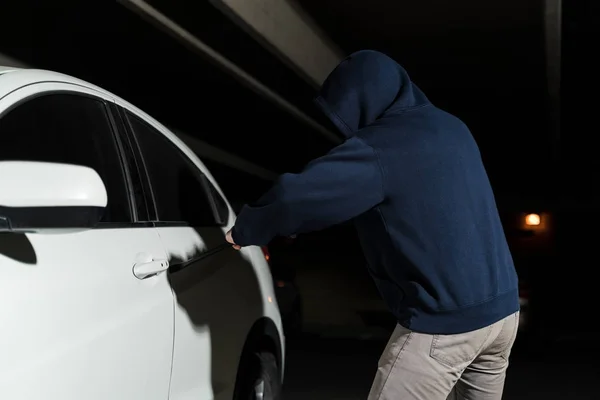 穿连帽衫的强盗企图在黑暗的停车场用撬棍撬开车门 — 图库照片