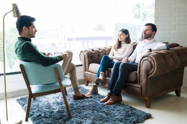 Ofiste psikologla konuşurken koltukta oturan mutsuz İspanyol çift.