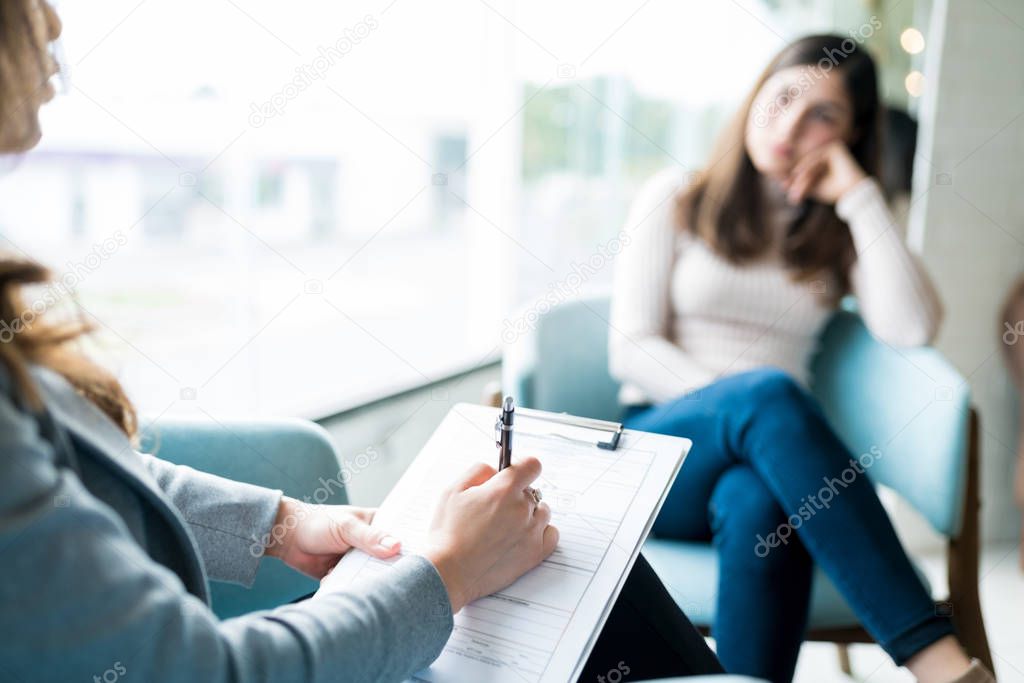 Female therapist writing on notepad while talking to patient at office during psychology treatment