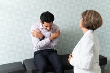 Ateşli İspanyol bir adam klinikte kontrol için kıdemli kadın doktoru ziyaret ediyor.