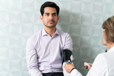 Kıdemli kadın doktor hastanede tansiyon ölçer ile adamı kontrol ediyor.