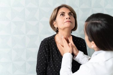 Caucasian woman visiting female geriatrician for thyroid checkup clipart